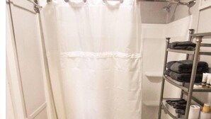 A bathroom with a shower curtain, a toilet, and a shelf with towels and toiletries.