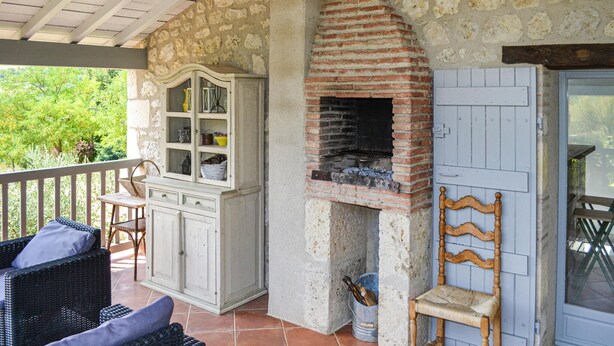 Eine rustikale Außenpatio mit Steinwand, Backofen aus Ziegeln, Korbmöbeln und einem Holzstuhl.