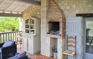 Eine rustikale Außenpatio mit Steinwand, Backofen aus Ziegeln, Korbmöbeln und einem Holzstuhl.