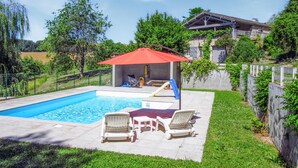 Ein Schwimmbecken mit Liegestühlen und einem roten Sonnenschirm, umgeben von einer Rasenfläche und Bäumen.