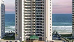 Um hotel com muitos andares, varandas múltiplas, área de piscina e vista para o oceano.