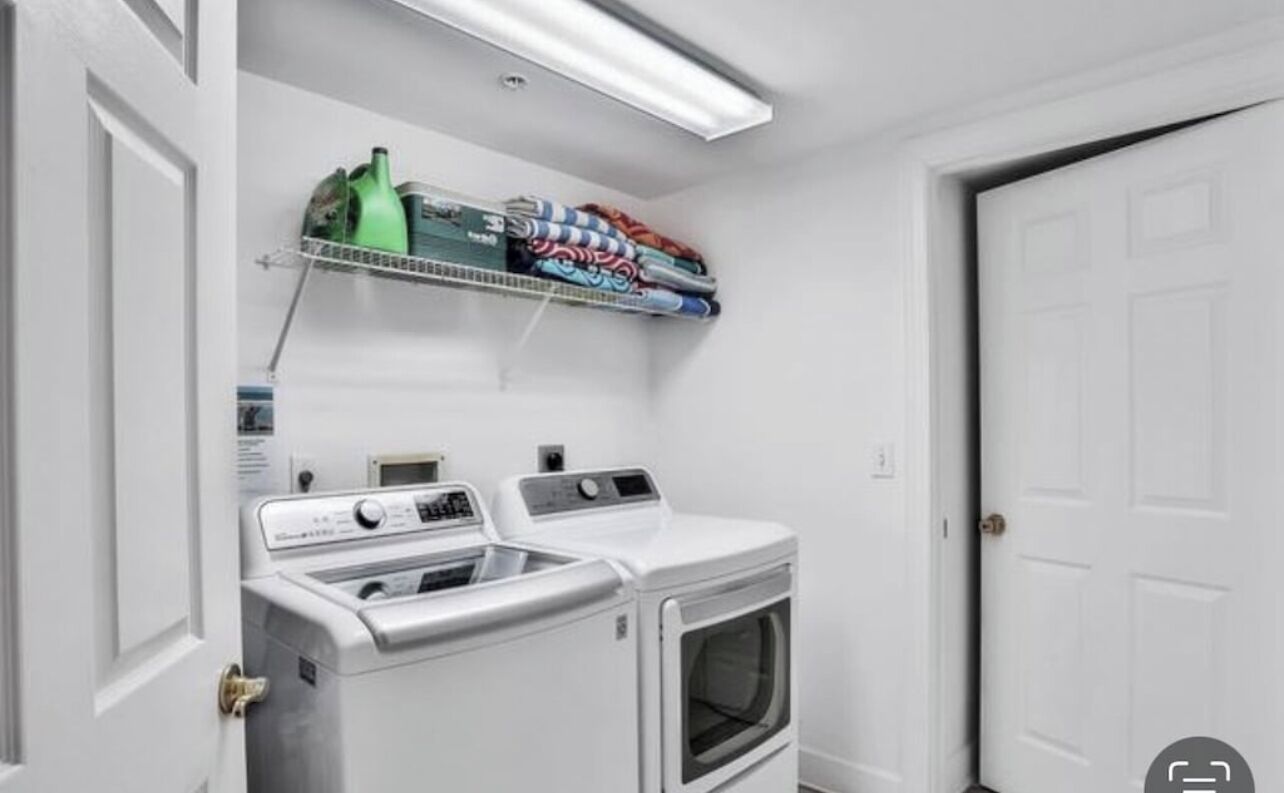 Een wasserij met twee voorladers en drogers, een plank met opgevouwen kleding en een plafondlamp.