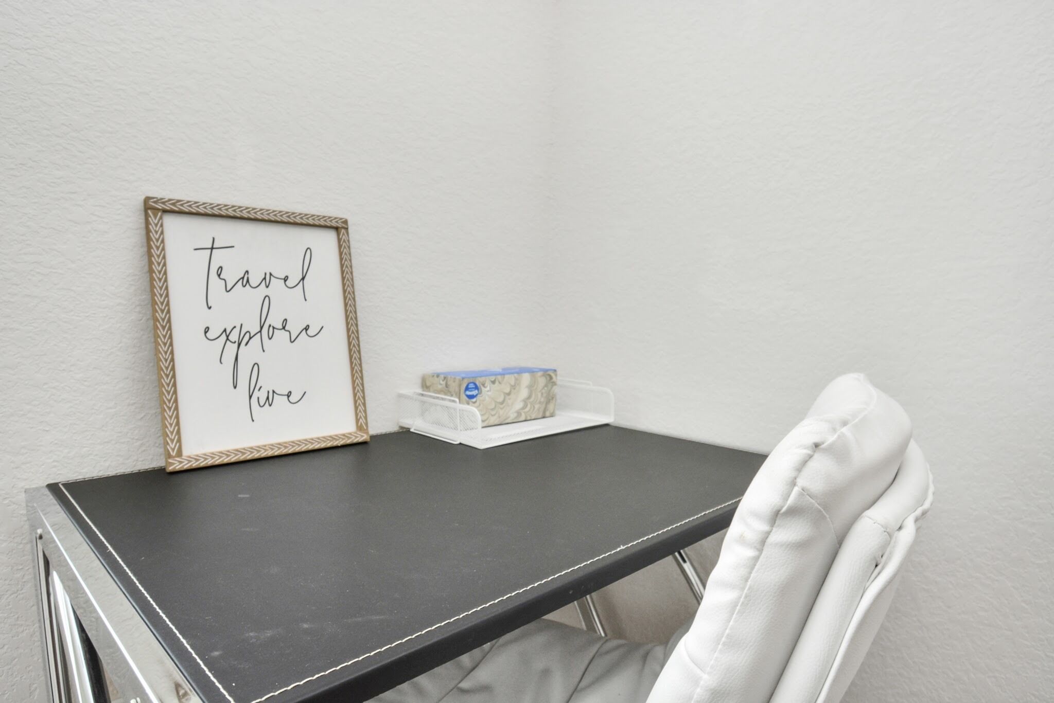 Une petite table sur laquelle est posé un panneau encadré avec l’inscription « voyage, découverte, cinq », ainsi qu’une chaise blanche.