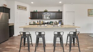 Una cocina moderna con armarios oscuros, un refrigerador de acero inoxidable, una isla central con taburetes de bar y un microondas encima de la isla.