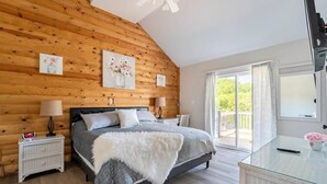Ein Schlafzimmer mit Holzboden, einem Bett mit grau-weißer Bettdecke, zwei Nachttischen mit Lampen, einem Beistelltisch und einem Glastisch mit einer Vase.