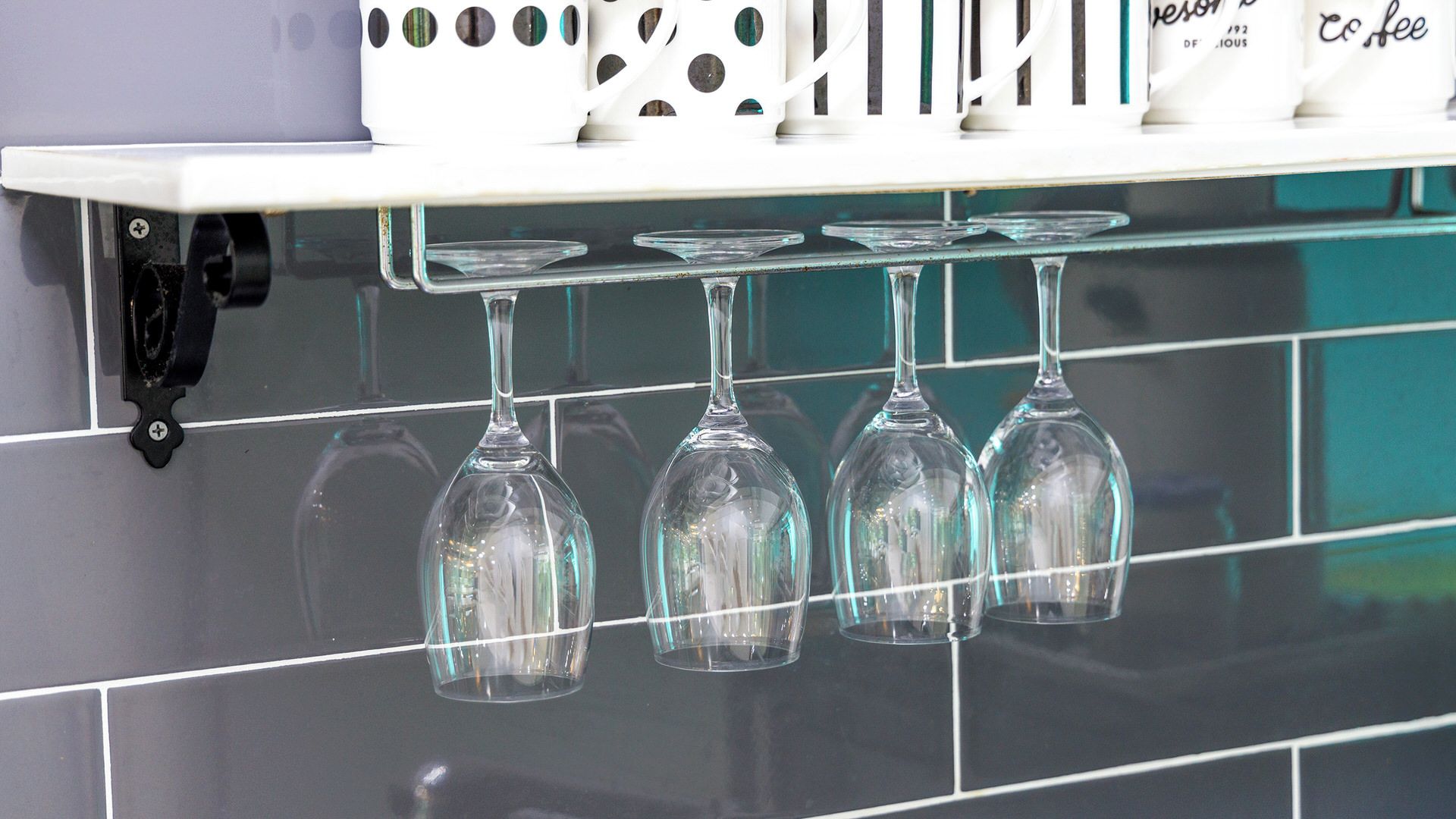 A kitchen with a white shelf holding a coffee maker and a row of wine glasses hanging from a rack.
