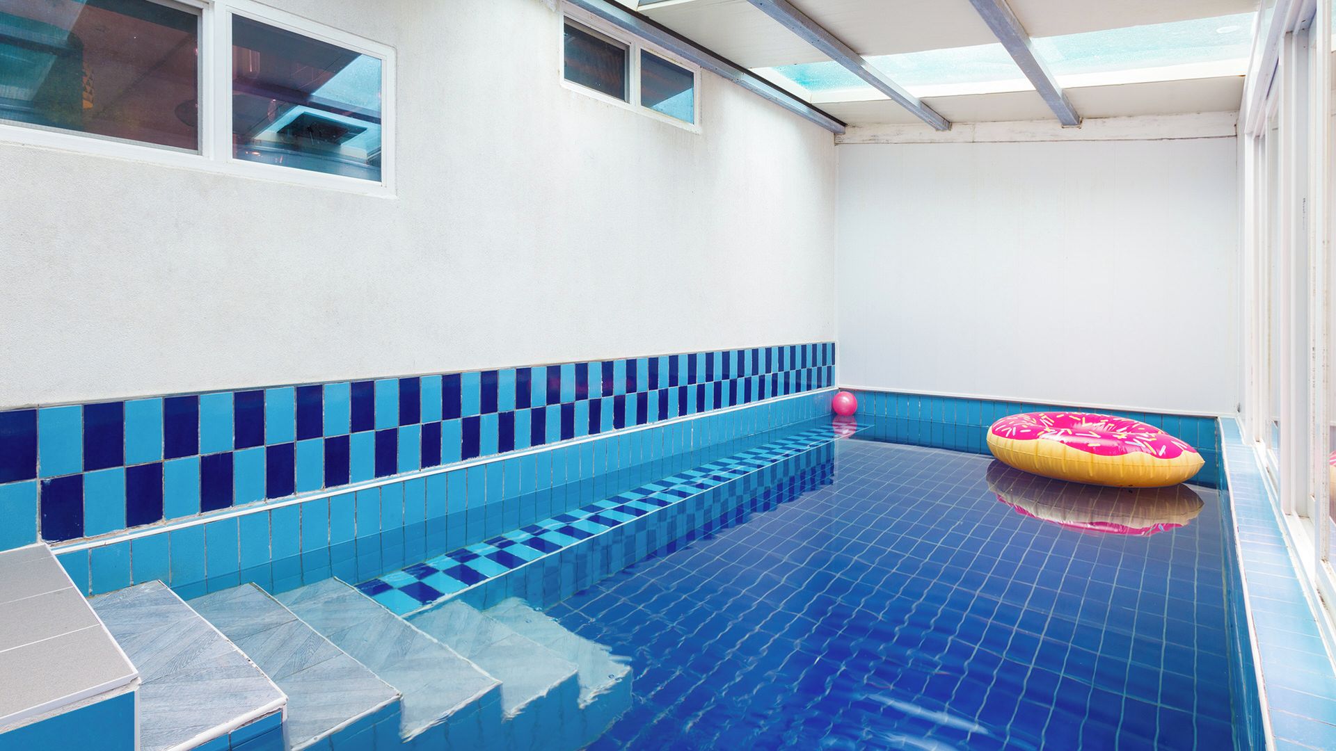 A swimming pool with blue tiles, a sunroof, and a pink inflatable ring.