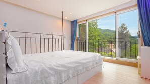 A bedroom with a bed, a window with a view of greenery, and a balcony with a railing. - Gapyeong Gamseong216 Poolvilla Pension (Gapyeong)