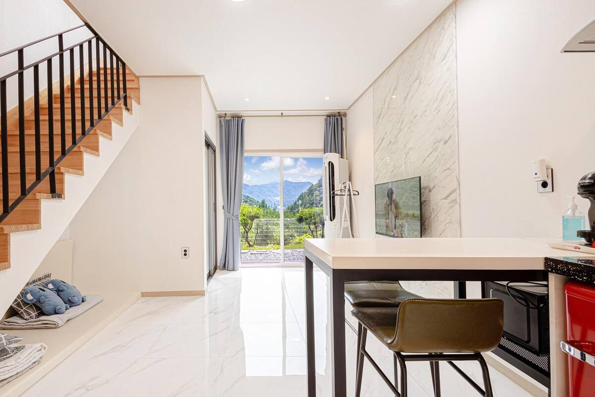 Eine moderne Küche mit Essbereich, einer Treppe mit Holzdielen und schwarzen Geländern sowie Bergblick durch das Fenster.