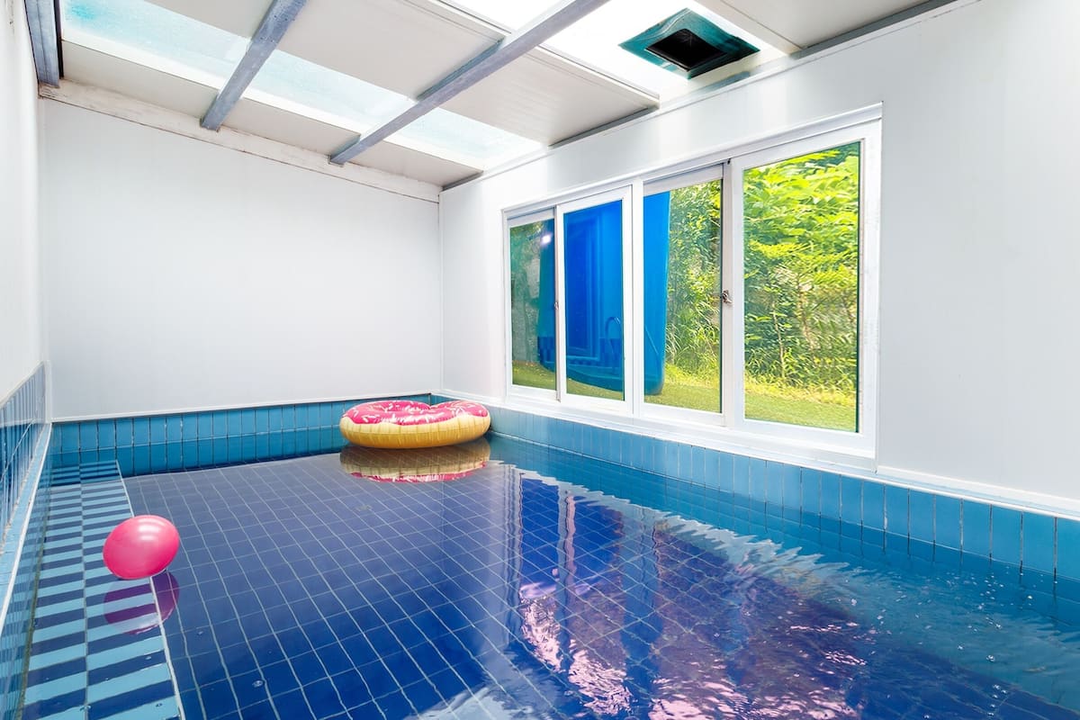 Ein Hallenbad mit hellblauen Fliesen, einem rosa Schwimmreifen und einem roten Ball.
