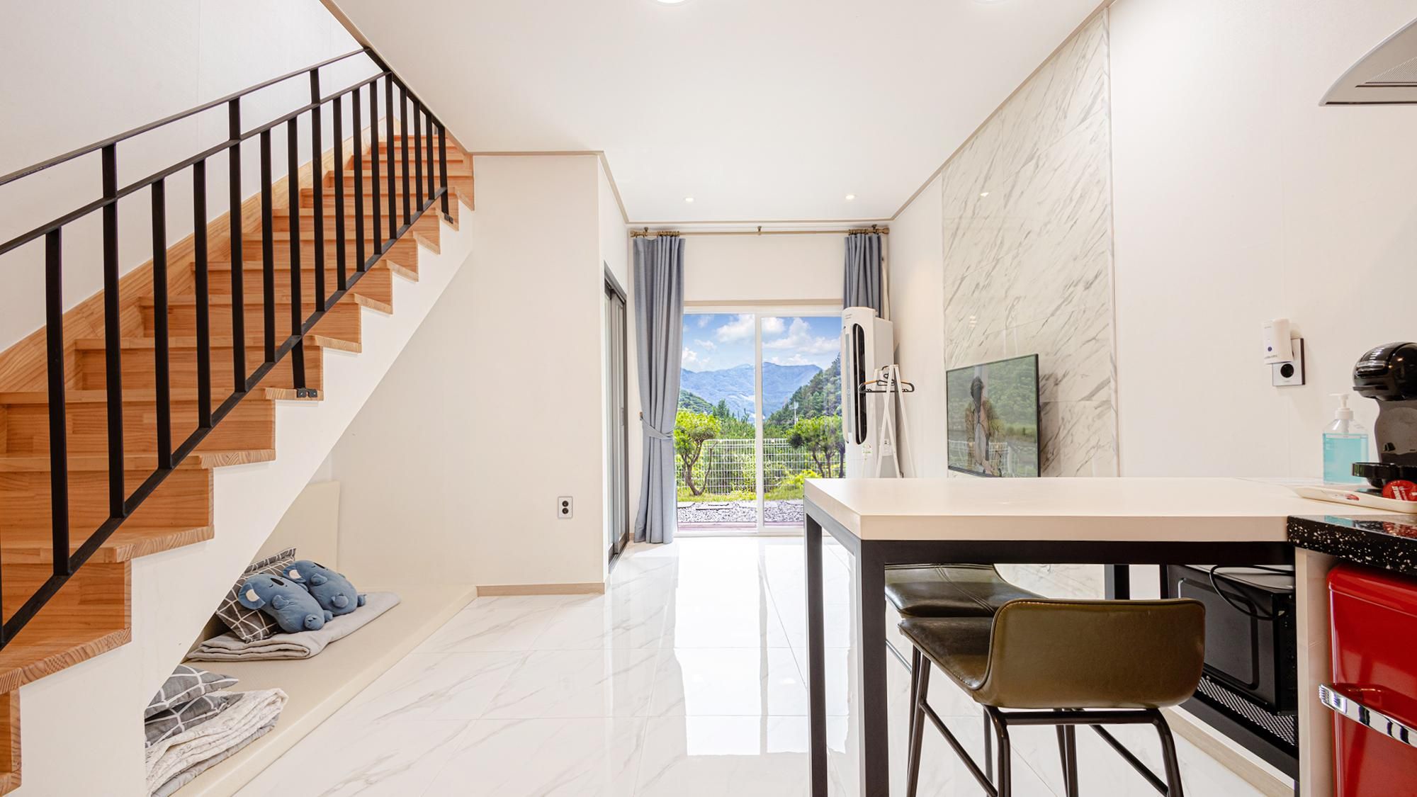 A modern kitchen with a dining area, a staircase, and a view of mountains through the window.