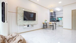 A modern living room with a large flat-screen TV mounted on a marble wall, a dining area with a table and chairs, and a kitchen in the background. - Gapyeong Gamseong216 Poolvilla Pension (Gapyeong)