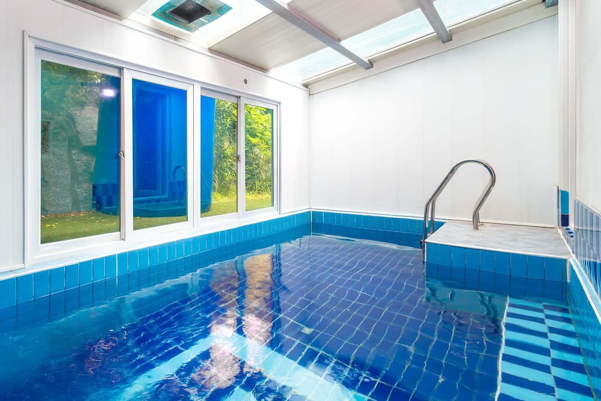 Ein Hallenbad mit großen Glaswänden, blauen Fliesen und einer Metallhandläufe.