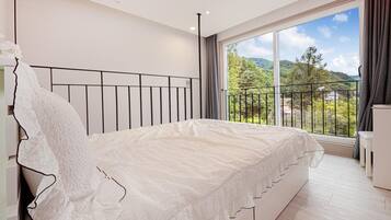 Ein Schlafzimmer mit einem großen Bett, Blick auf Grünflächen und Hügel vom Balkon aus, und einem modernen Design.
