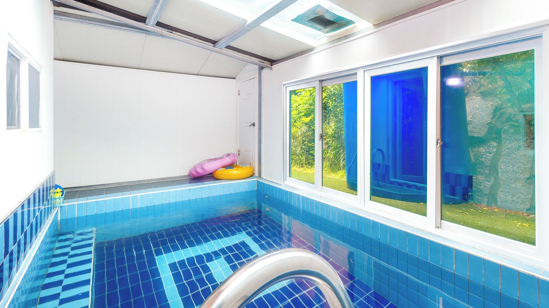 A swimming pool with blue tiles, a window with a view of greenery, and a door.