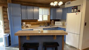 Eine Küche mit blauen Schränken, einem weißen Kühlschrank, einer Mikrowelle und einer Kaffeemaschine. An der Kücheninsel stehen zwei Hocker.