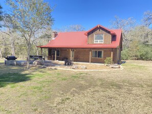 A log cabin with a red roof, a chimney, and a porch with outdoor seating. - Paradise at Bucek Lane (Schulenburg)