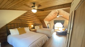 Ein gemütliches Schlafzimmer im Dachgeschoss mit zwei Betten, Holzbalken an der Decke und einem Deckenventilator.