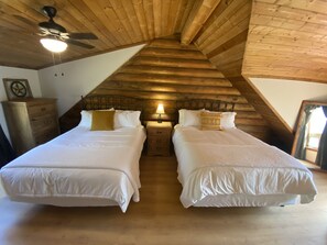 A bedroom with two beds, wooden ceiling beams, a ceiling fan, and a nightstand with a lamp. - Paradise at Bucek Lane (Schulenburg)
