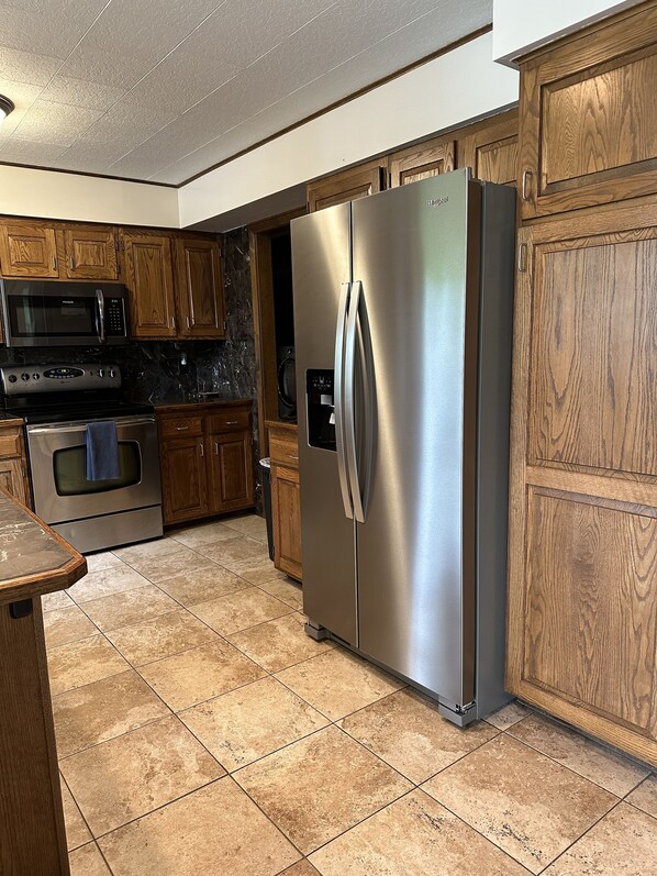 A kitchen with wooden cabinets, a stainless steel refrigerator, a built-in microwave, and a dishwasher. - Grandpa’s Lagoon! Spacious Cabin on Eagle River Chain, minutes from downtown! (Eagle River)