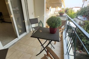 Un balcón con una mesa y sillas, una planta en maceta y vistas a la calle y al verdor.