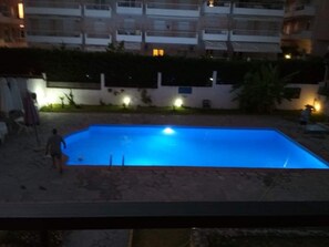 Una piscina con borde de baldosas, rodeada por un muro bajo y un seto.