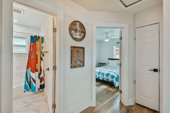 A hallway with a shower, a bed with a blue and white patterned bedspread, and a wooden wall decoration.