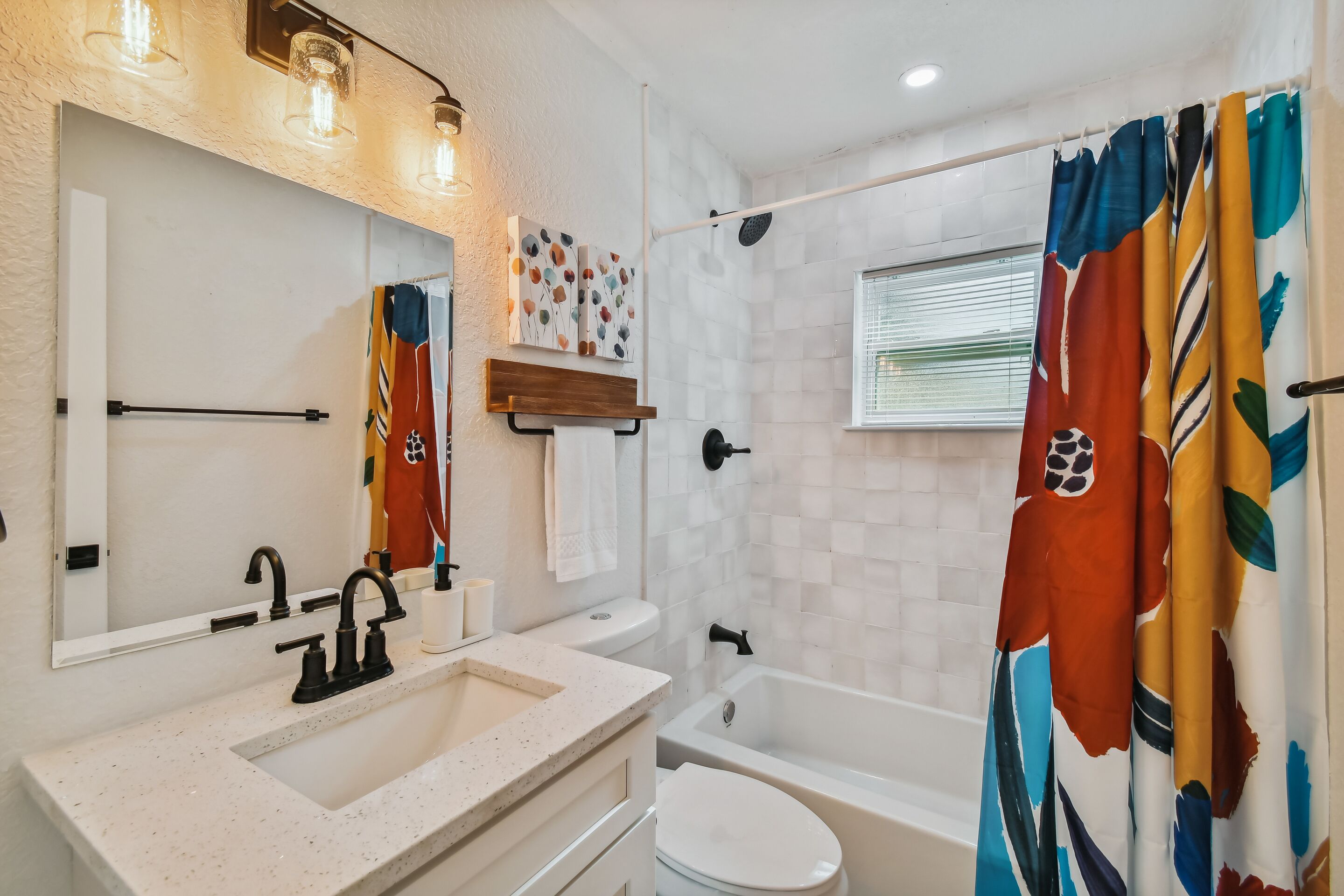 A bathroom with a sink, toilet, and bathtub. There is a mirror above the sink and a shower curtain with a floral pattern.