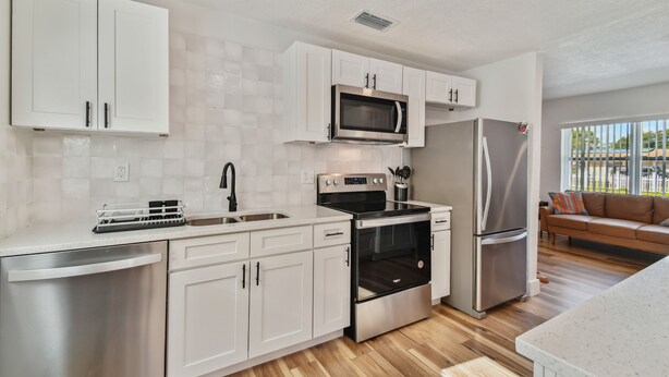 A modern kitchen with white cabinets, stainless steel appliances, and a wooden floor. - Charming Centrally Located, 3 bedroom house! (Tampa)