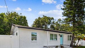A small, single-story house with a white exterior, a blue door, and a fenced yard. - Charming Centrally Located, 3 bedroom house! (Tampa)
