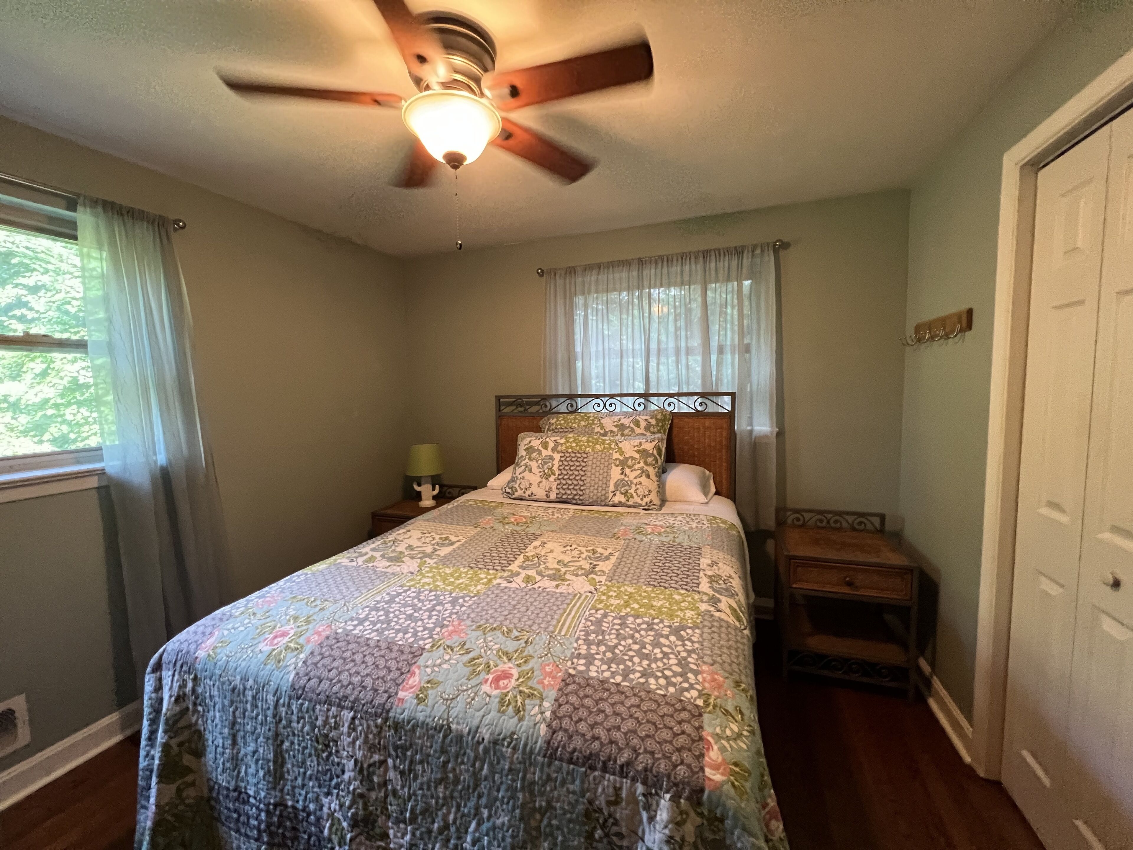 A bedroom with a bed, a nightstand, a ceiling fan, and a window with curtains.