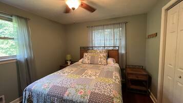 A bedroom with a bed, a nightstand, a ceiling fan, and a window with curtains.