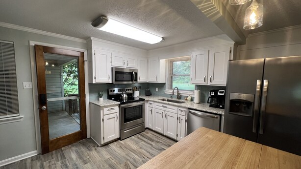 A modern kitchen with white cabinets, stainless steel appliances, and a wooden dining table. - Cheerful, relaxing ranch in quiet neighborhood with fire pit (Newton)