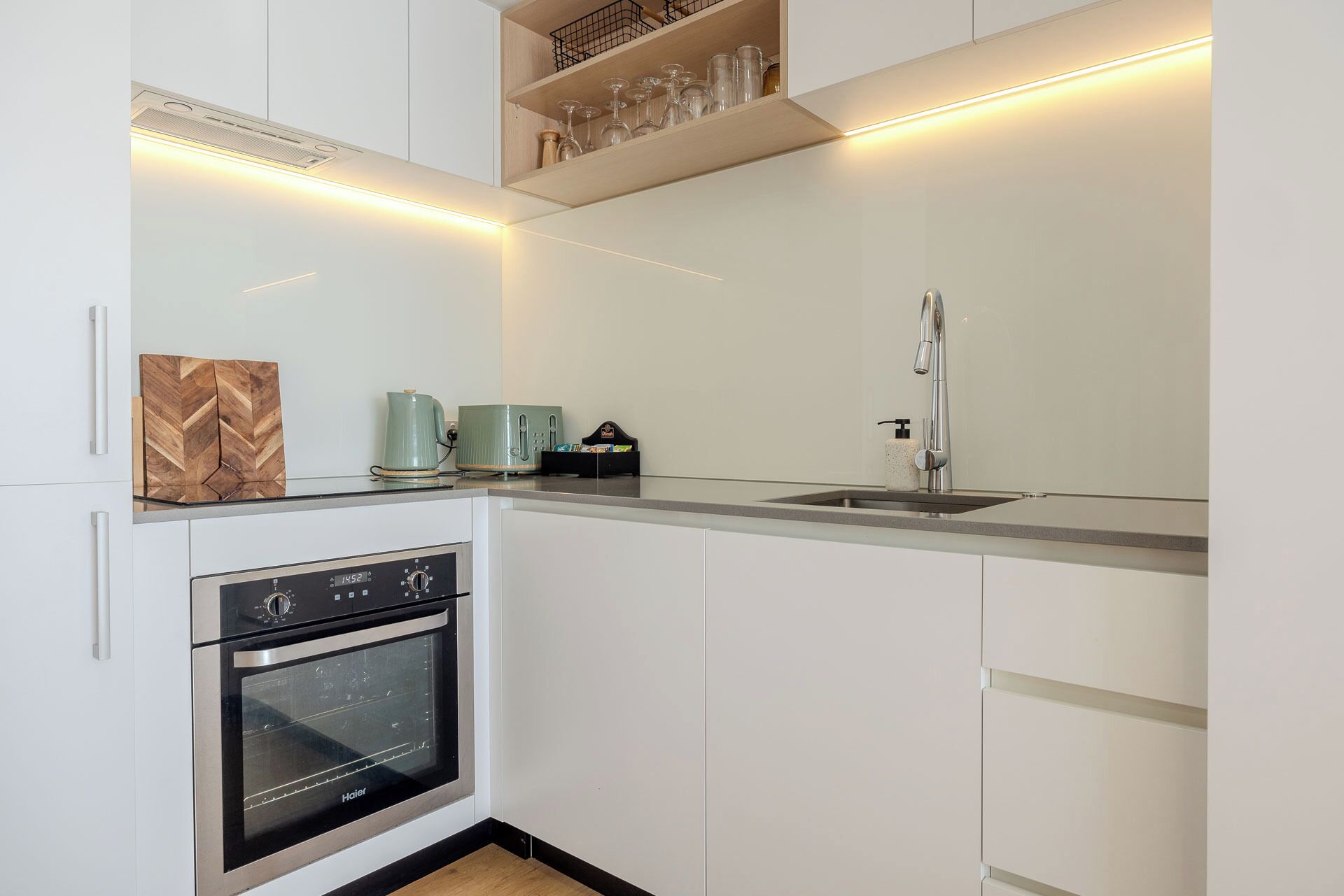 A modern kitchen with white cabinetry, a stainless steel oven, a sink, and a countertop with a kettle and toaster.