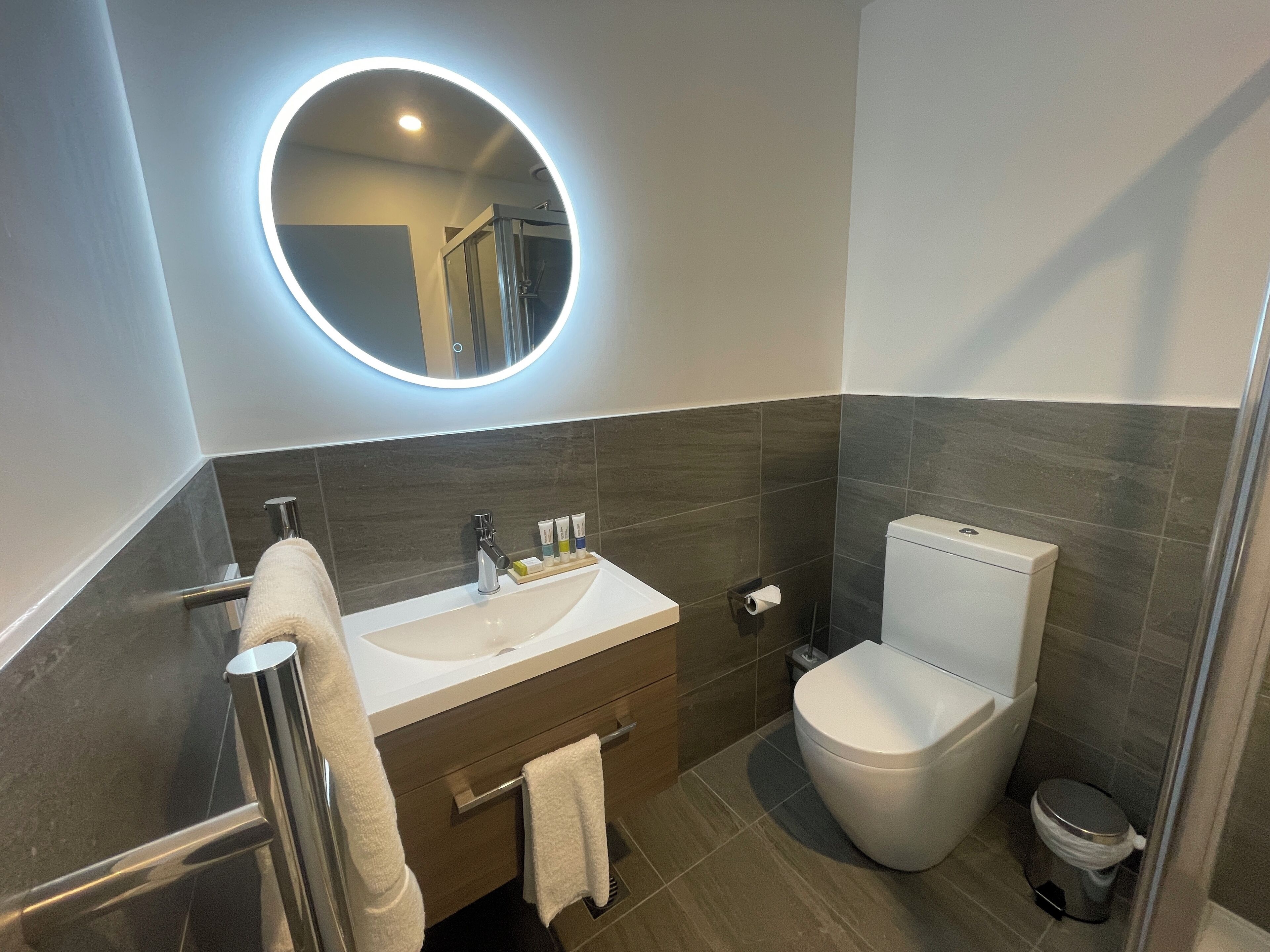 A modern bathroom with a round mirror, white sink, and toilet.