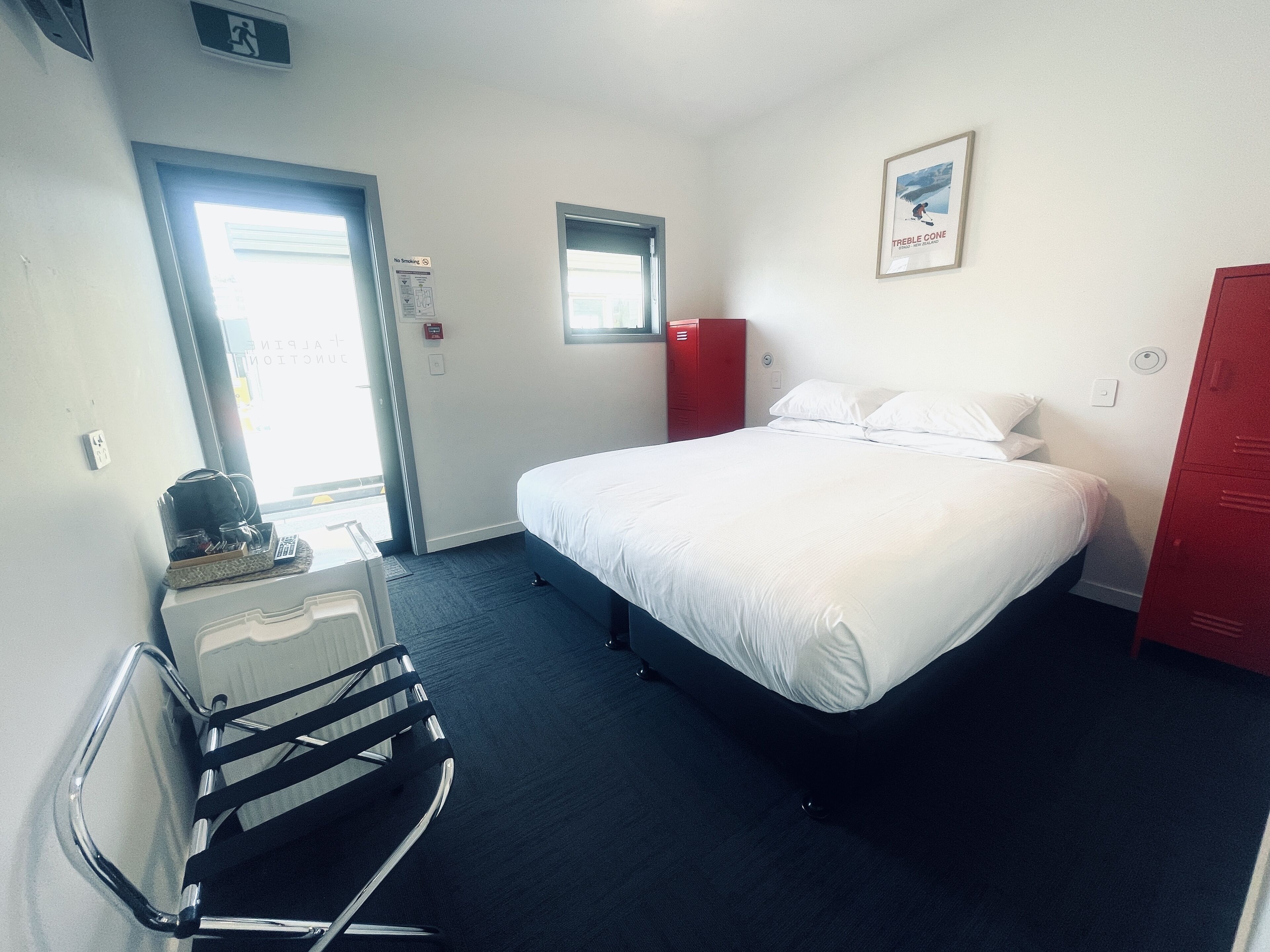 Una habitación de hotel con cama, escritorio, silla, armario rojo y ventana.