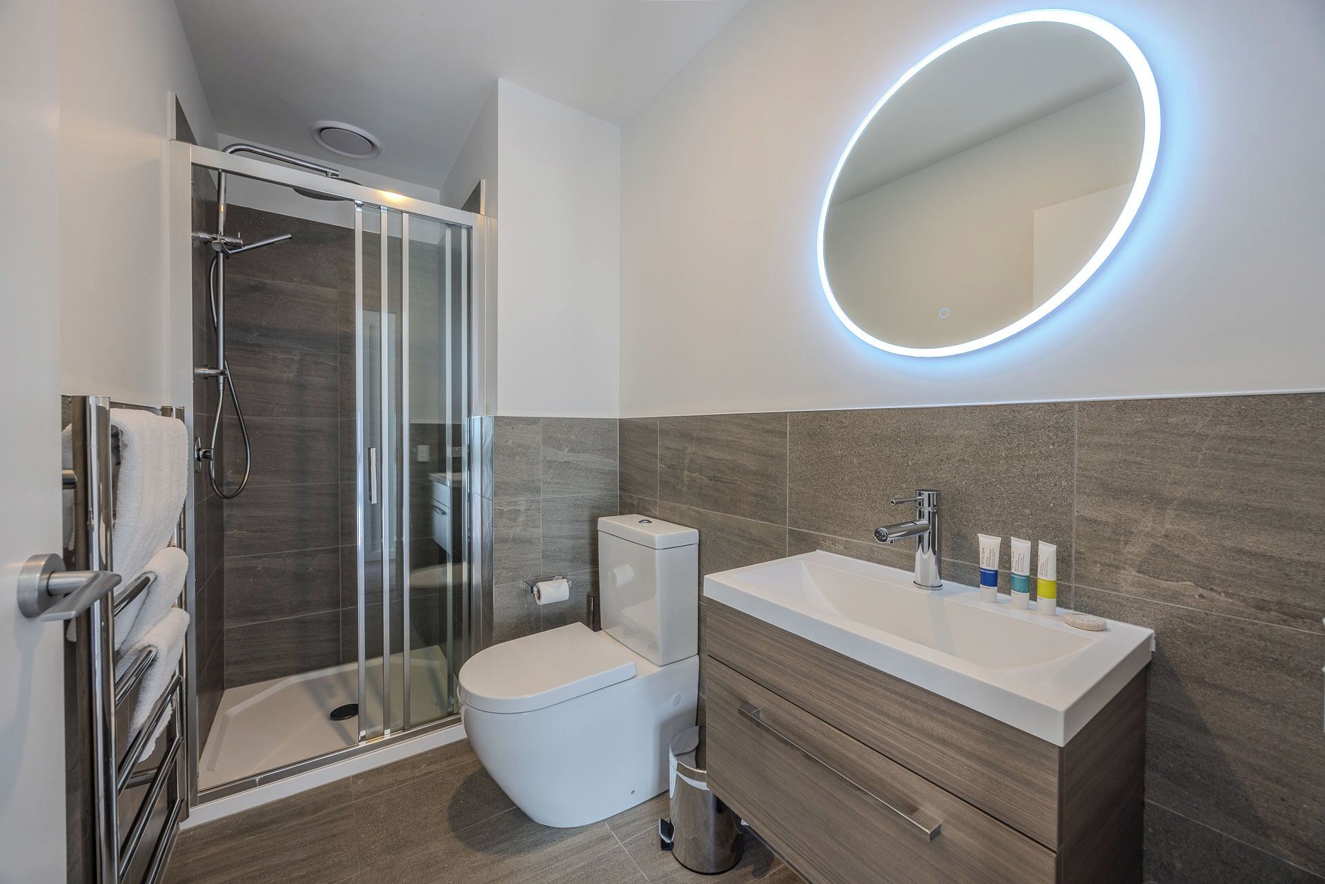Een moderne badkamer met een douchecabine van glas, een toilet, een wastafel met spiegel en toiletartikelen.