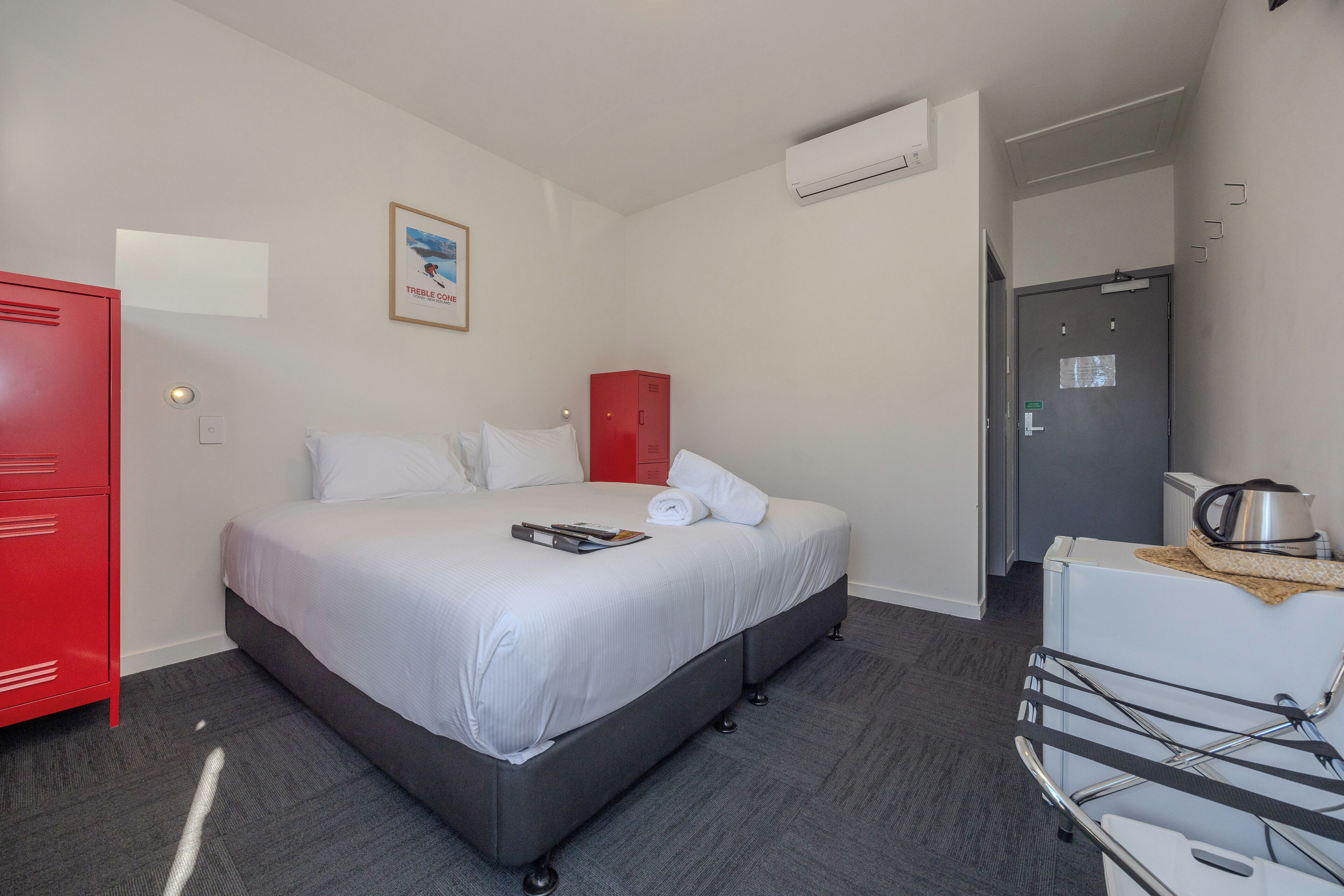 Una habitación de hotel con una cama, un armario rojo, un mueble blanco y una zona de kitchenette.