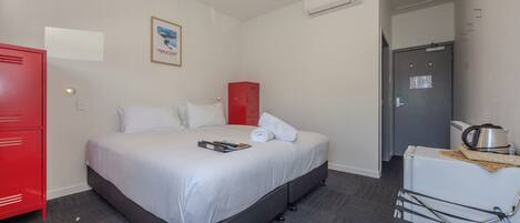 Una habitación de hotel con una cama, un armario rojo, un mueble blanco y una zona de kitchenette.