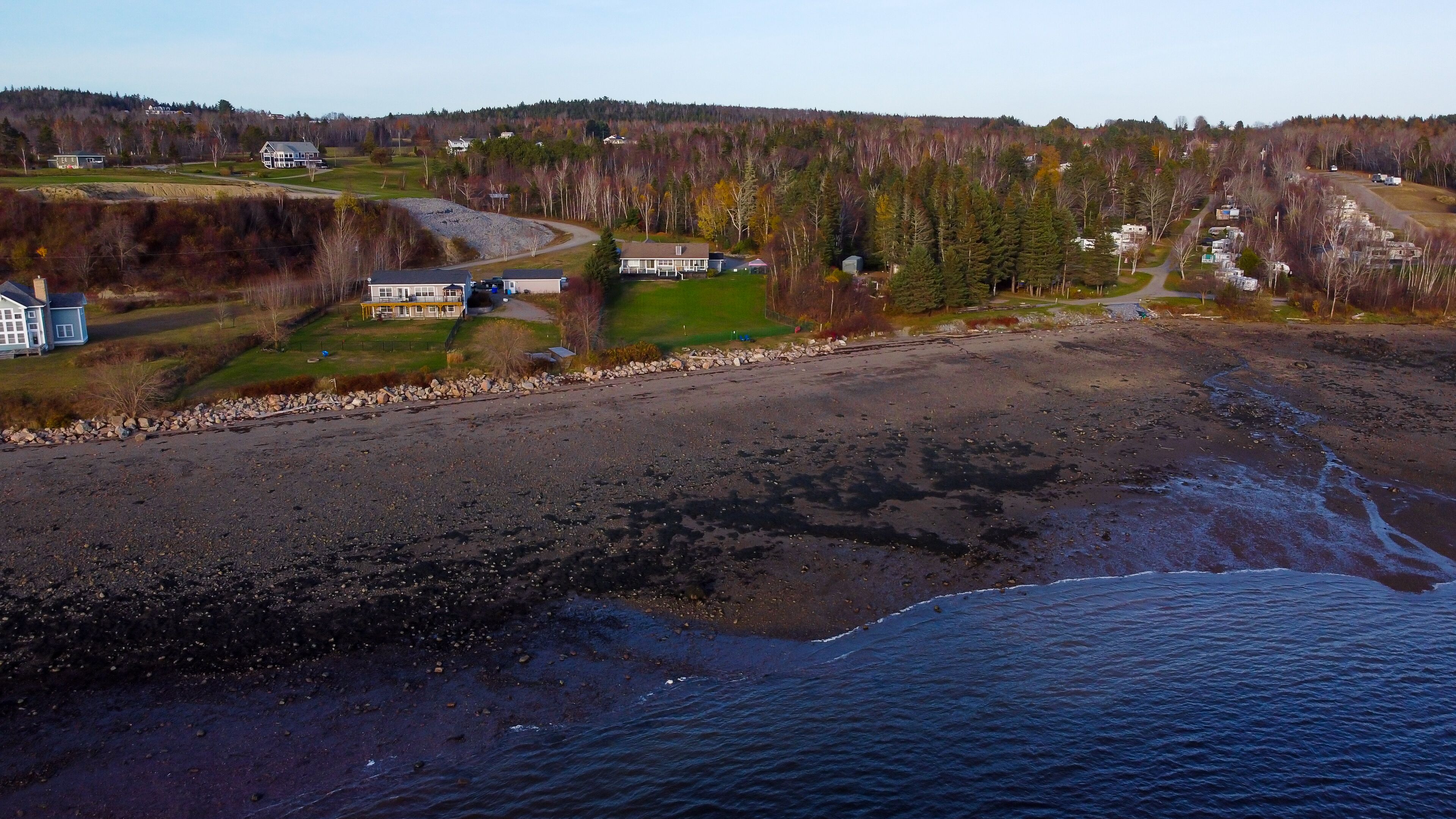 A coastal area with a rocky beach, houses, and a forested hill in the background.