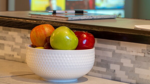 A white bowl with a textured pattern containing three apples and a pear on a kitchen counter.
