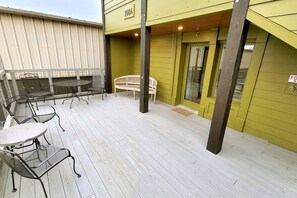 A covered outdoor patio with metal and wicker furniture, a wooden bench, and a door with a fire safety sign. - Custom Shed #1 in Berry Hill off 8th—Step-Free (Nashville)