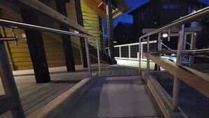 Ulkoterassi, jossa on puinen lattiapinta, metallikaiteet ja portaikko, joka johtaa rakennukseen.