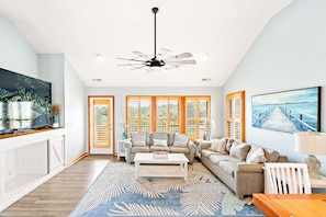 A spacious living room with a large window, a ceiling fan, and a television on a cabinet.