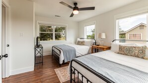 Un dormitorio con dos camas, ventilador de techo y ventanas amplias.