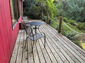 Eine Holzterrasse mit Tisch und Stühlen, umgeben von einem Seilabfangnetz und üppiger Vegetation.