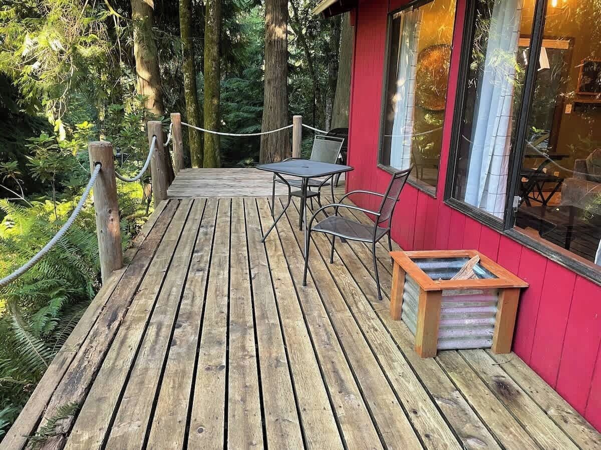 Eine Holzterrasse mit Tisch und Stühlen, umgeben von einem Seilgeländer und Bäumen.