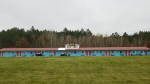 A motel with a red roof and blue exterior walls, featuring multiple rooms with red doors and windows, and a parking area in front. - Richard Lake Motel (Sudbury)