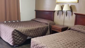 A hotel room with two queen beds, a wooden headboard, a nightstand, two wall-mounted lamps, and a framed picture on the wall.