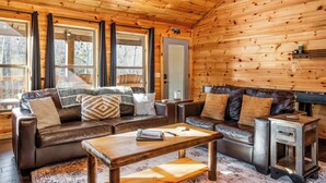 Ein gemütliches Blockhaus-Interieur mit einer braunen Ledersofa-Garnitur, einem Holztisch und einem kleinen Beistelltisch.